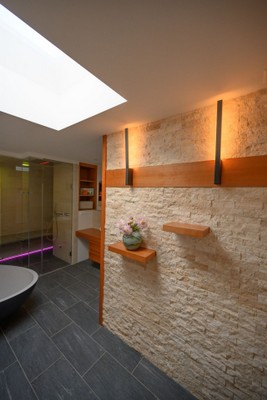 Umgebautes Bad mit heller Natursteinwand, Dusche und Dachfenster